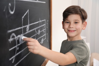 Photo of Little boy writing music notes on blackboard in classroom