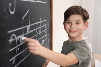 Little boy writing music notes on blackboard in classroom