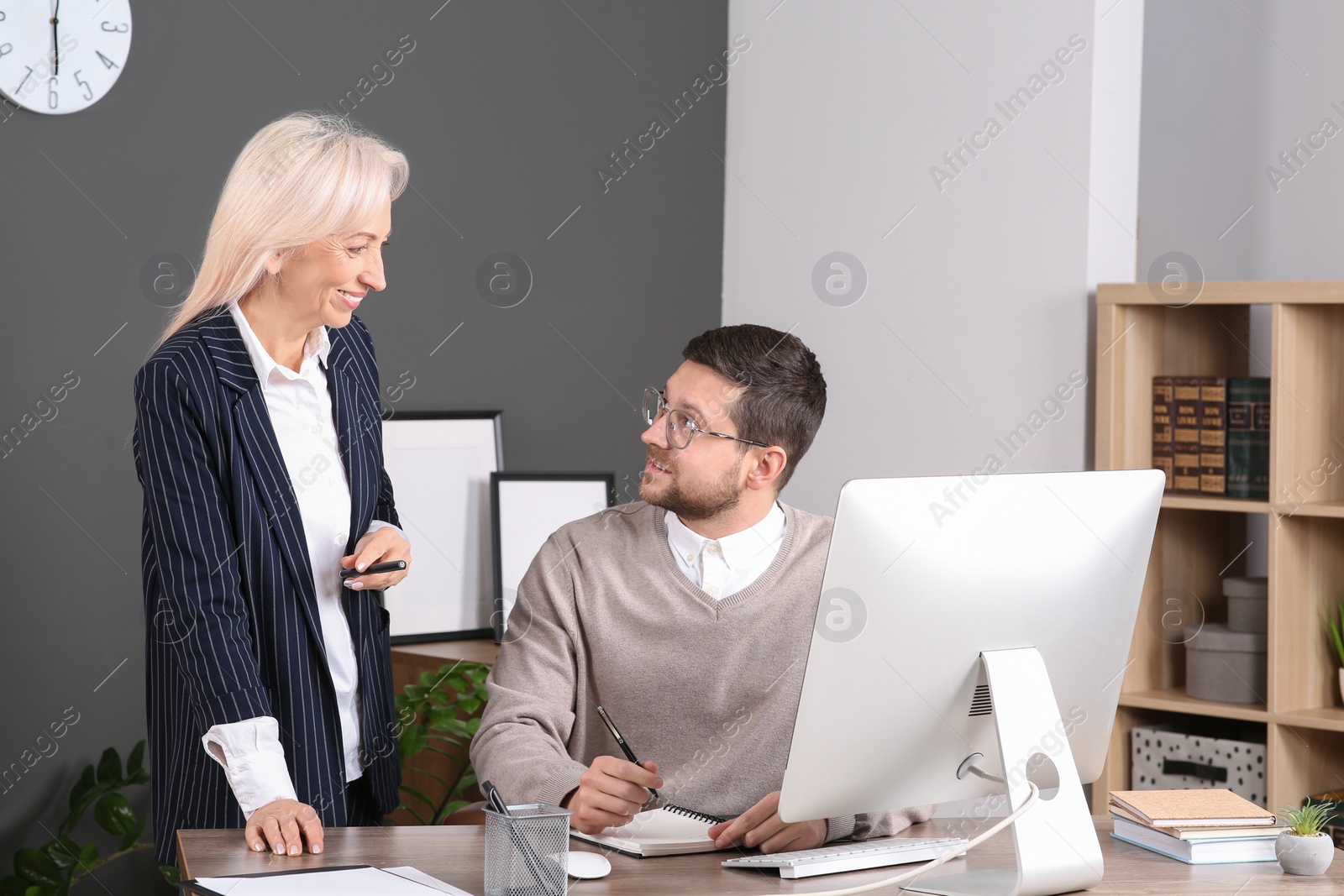 Photo of Boss and employee with notebook at wooden table in office