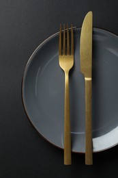 Photo of Elegant golden cutlery and plate on black background, top view