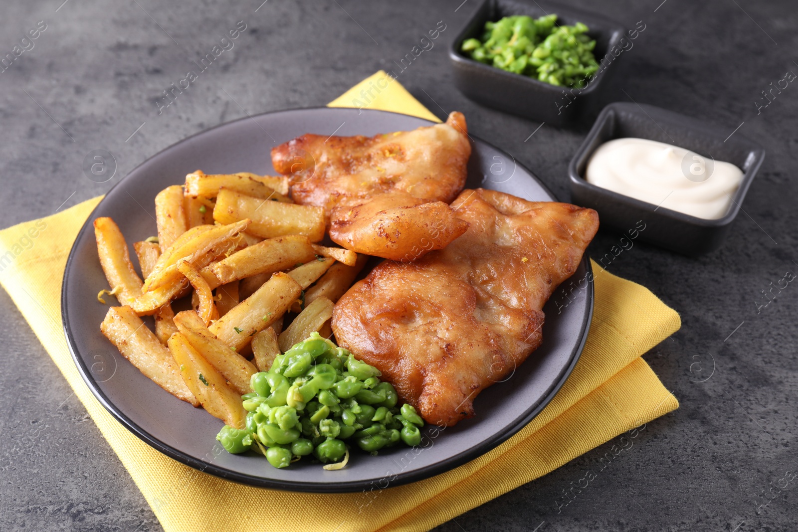 Photo of Tasty fish, chips, sauce and peas on grey table, closeup