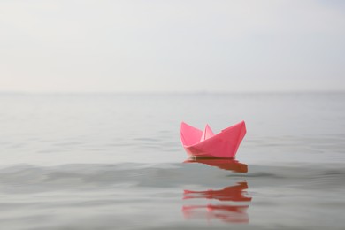 Photo of Pink paper boat on water surface, space for text