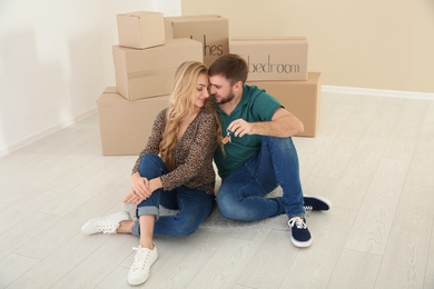 Photo of Happy young couple with key from their new house and boxes indoors