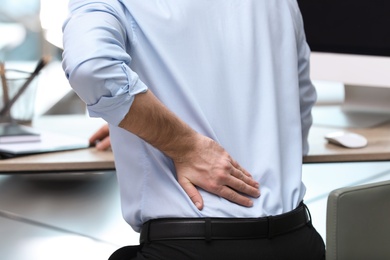 Photo of Businessman suffering from back pain at workplace, closeup