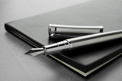 Photo of Stylish fountain pen, cap and leather notebook on light grey textured table, closeup