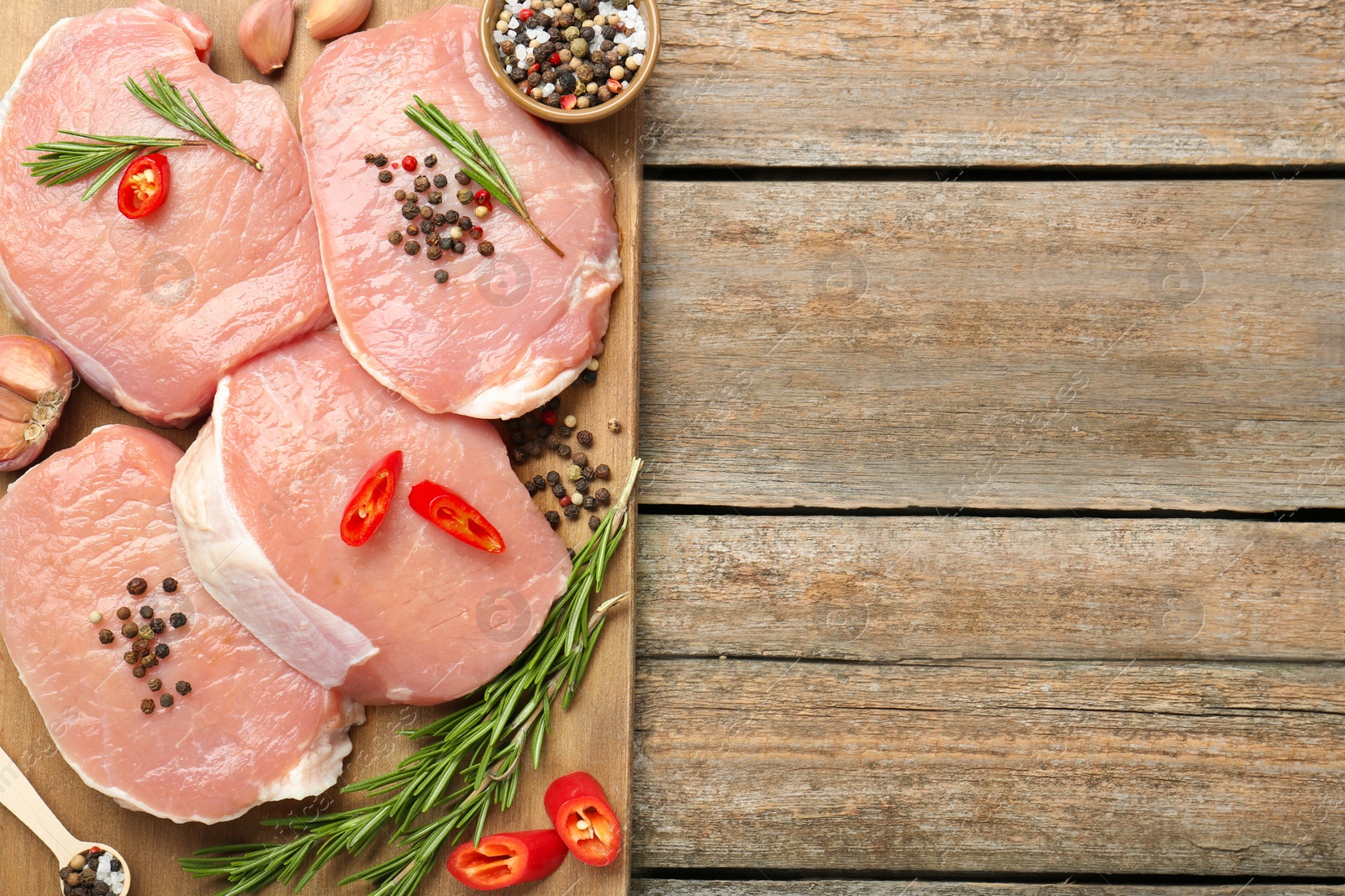 Photo of Pieces of raw pork meat and spices on wooden table, top view. Space for text