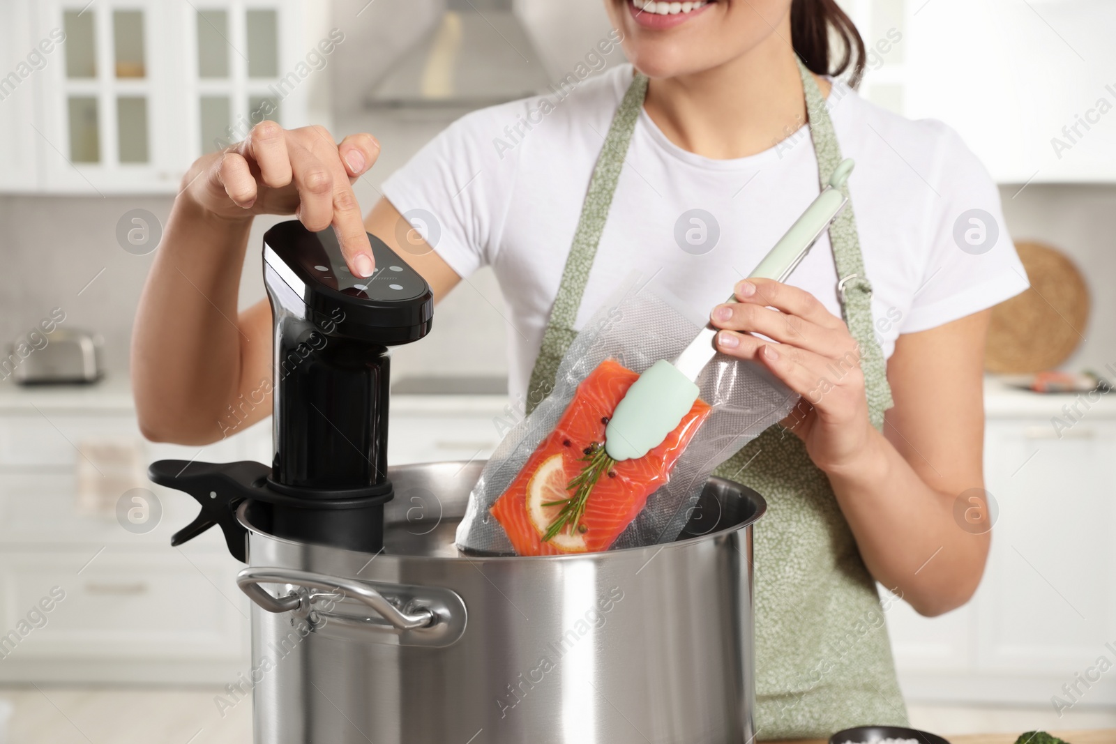 Photo of Woman putting vacuum packed salmon into pot and using thermal immersion circulator in kitchen, closeup. Sous vide cooking