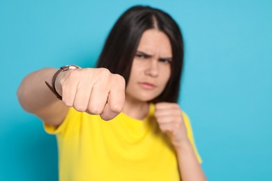 Photo of Young woman ready to fight against light blue background, focus on hand. Space for text
