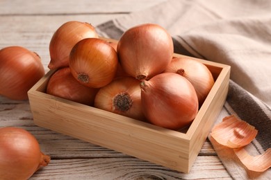 Crate with ripe onions on white wooden table, closeup