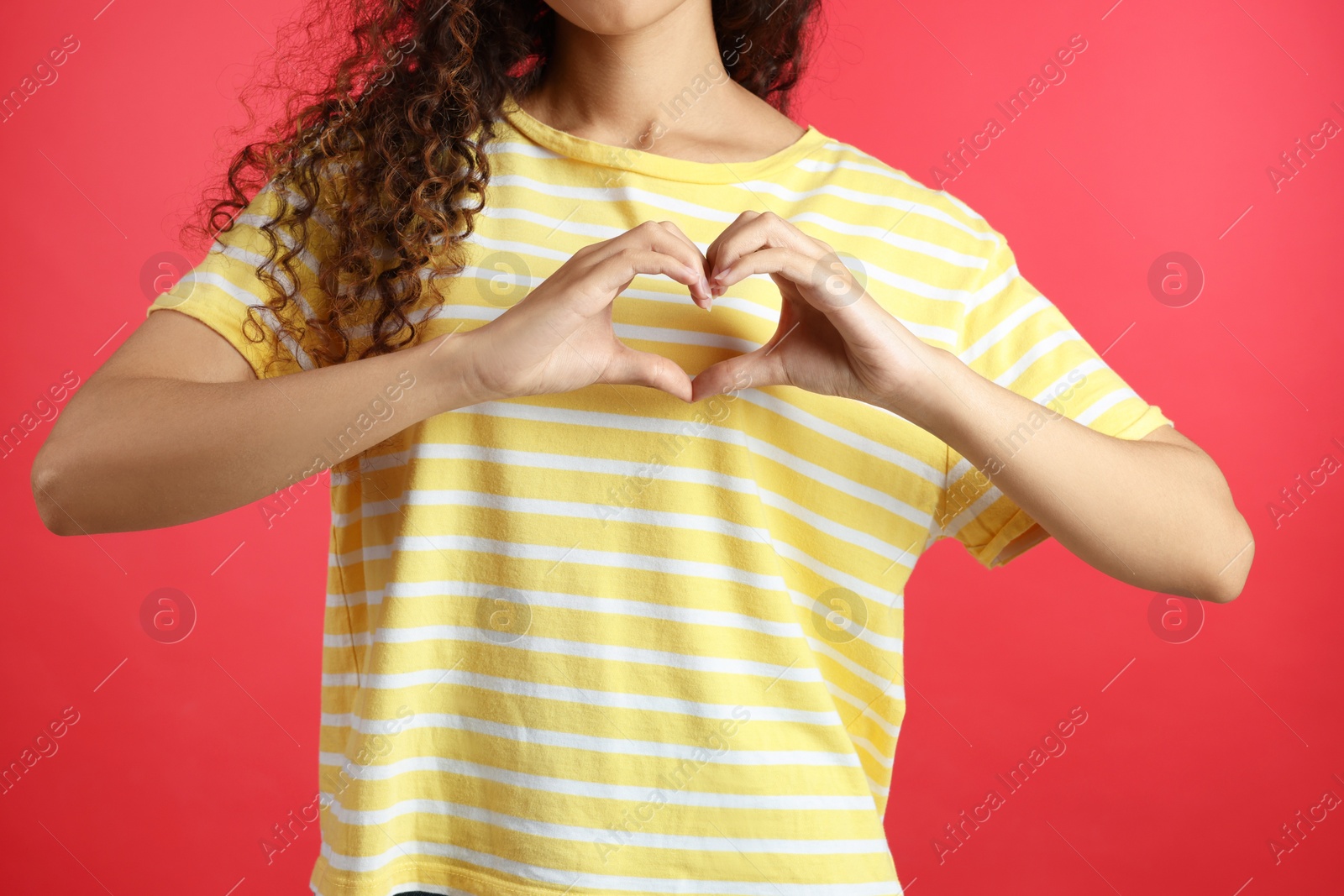 Photo of African-American woman making heart with hands on red background, closeup