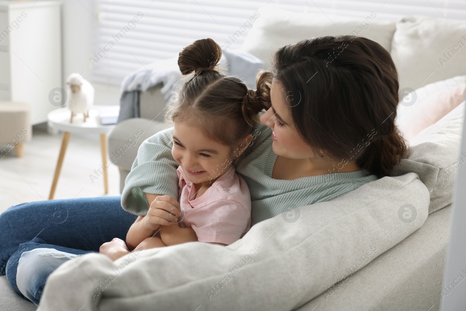 Photo of Young mother and her daughter spending time together on sofa at home