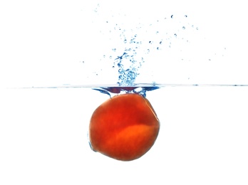 Fresh ripe peach falling in water on white background