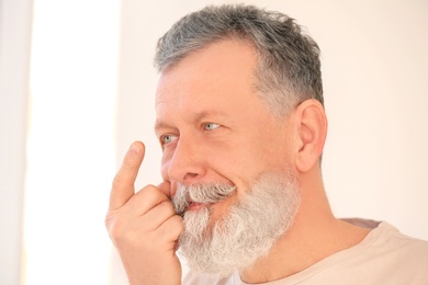 Photo of Senior man putting contact lens in his eye on light background