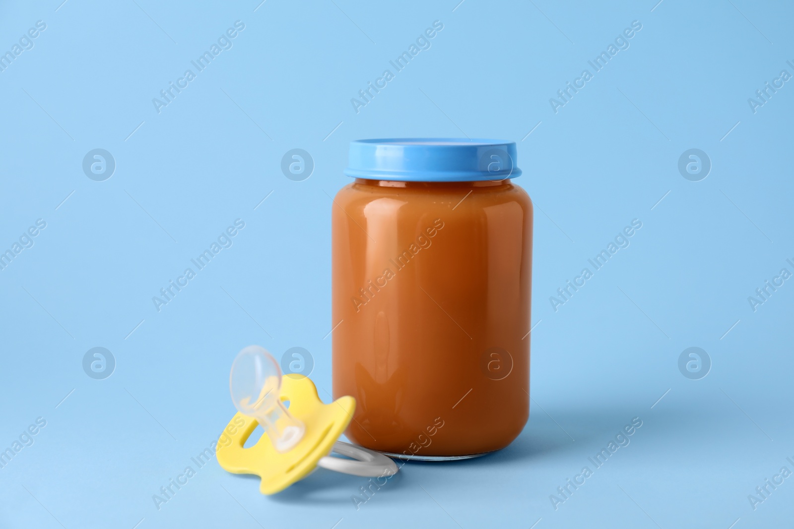 Photo of Healthy baby food and pacifier on light blue background