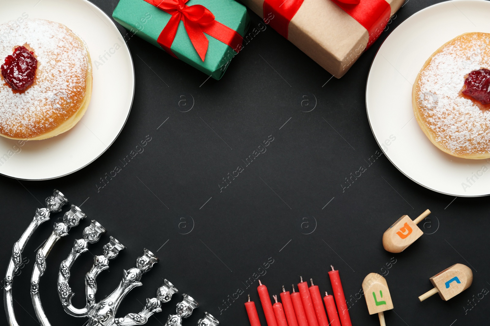Photo of Hanukkah traditional menorah, candles, doughnuts, dreidels with letters He, Pe, Nun, Gimel on black background, flat lay. Space for text