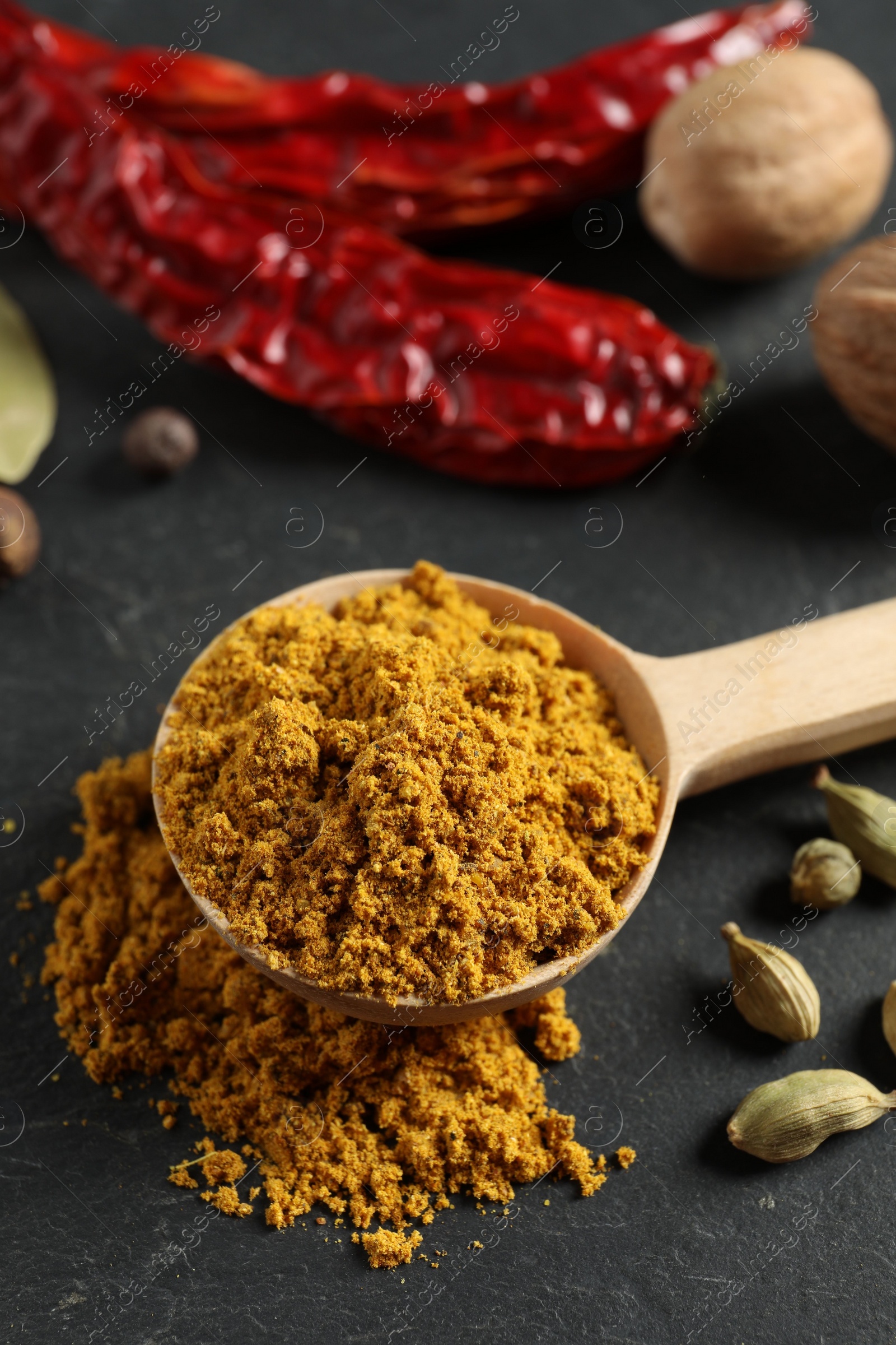 Photo of Spoon with dry curry powder and other spices on dark textured table, closeup