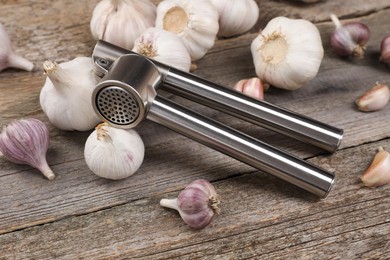 Photo of Garlic press and bulbs on wooden table. Kitchen utensil