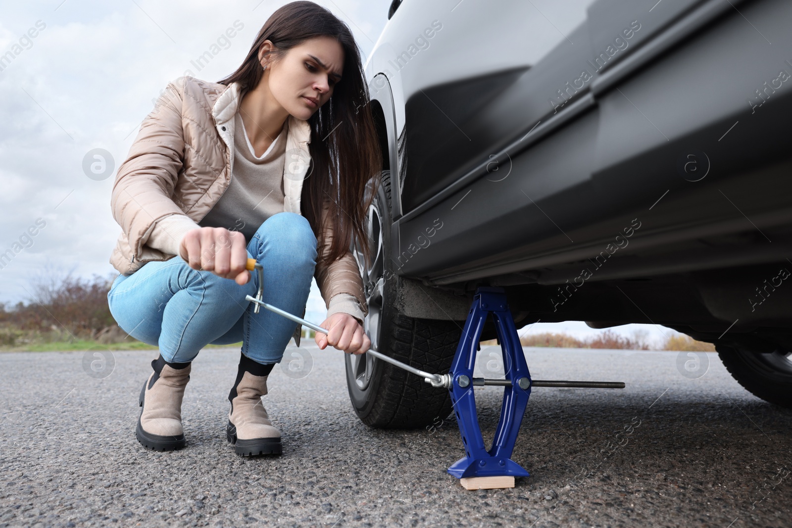 Photo of Young woman changing tire of car on roadside