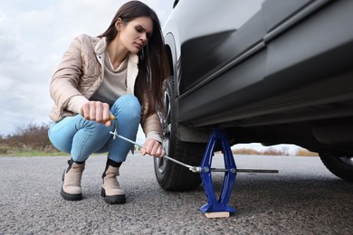 Young woman changing tire of car on roadside