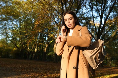 Emotional woman checking time while talking on smartphone in park. Being late concept