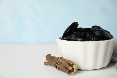 Photo of Tasty black candies and dried sticks of liquorice root on white table. Space for text