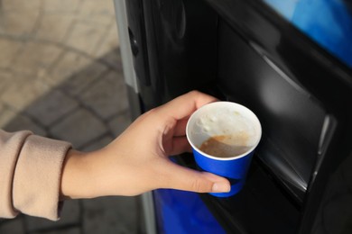 Photo of Woman taking paper cup with coffee from vending machine outdoors, closeup