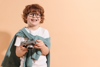 Fashion concept. Stylish boy with vintage camera on pale orange background. Space for text