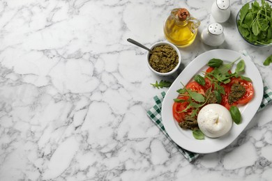 Photo of Delicious burrata salad with tomatoes, arugula and pesto sauce served on white marble table, flat lay. Space for text