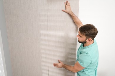 Photo of Man hanging stylish wall paper sheet indoors. Space for text