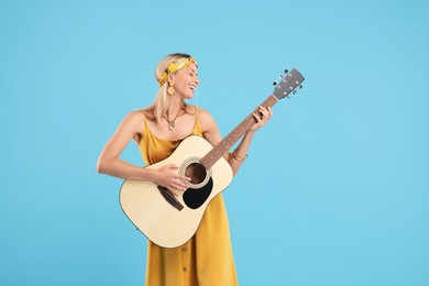 Happy hippie woman playing guitar on light blue background