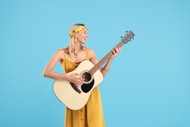 Photo of Happy hippie woman playing guitar on light blue background