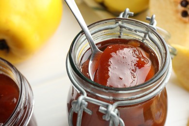 Taking tasty homemade quince jam from jar on blurred background, closeup