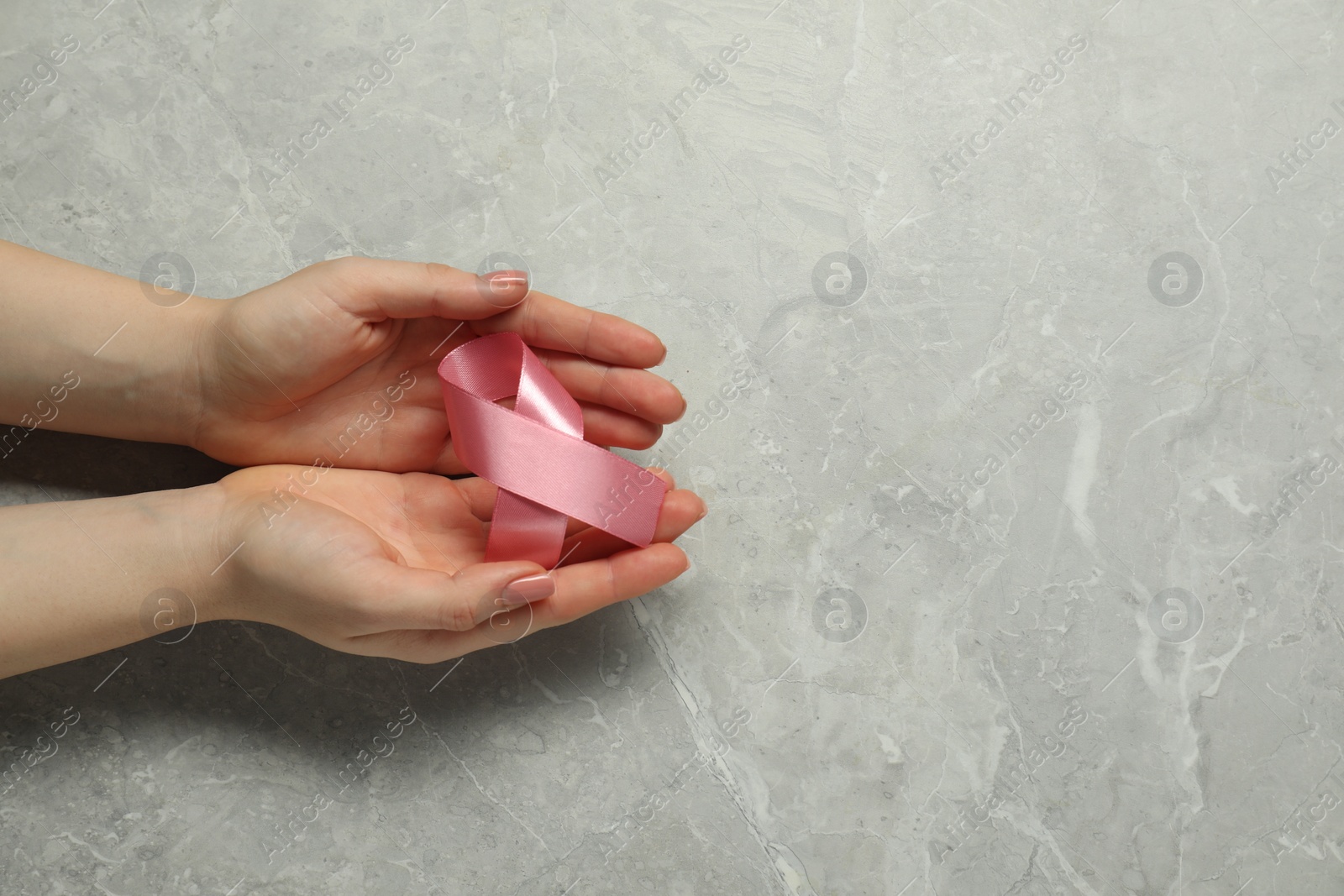 Photo of Breast cancer awareness. Woman with pink ribbon at grey marble table, top view. Space for text