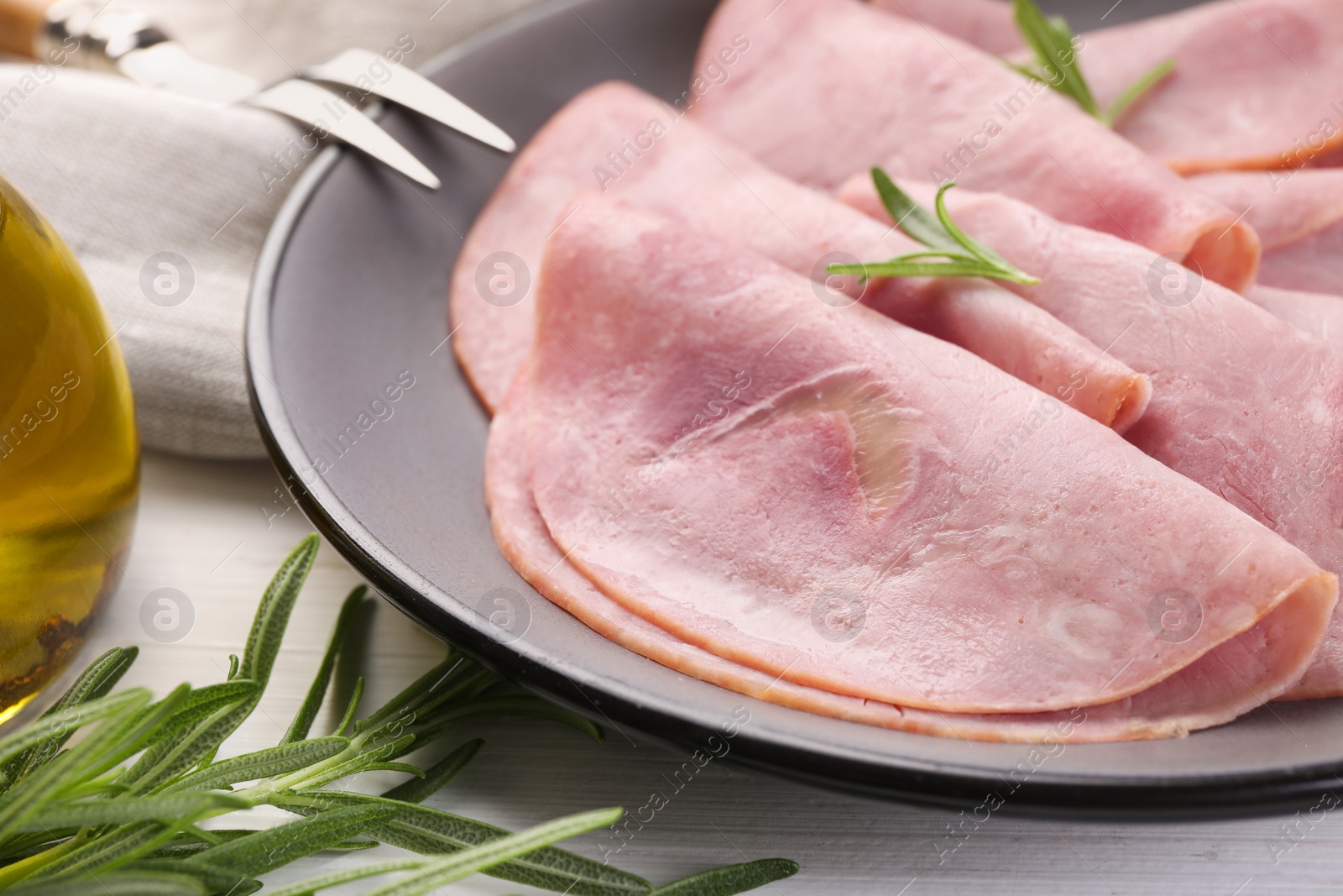 Photo of Tasty ham with rosemary and carving fork on table, closeup