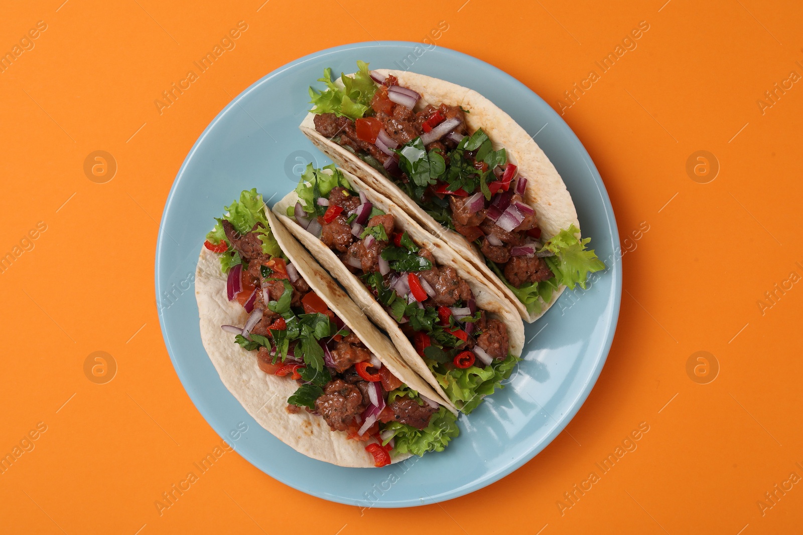 Photo of Delicious tacos with meat and vegetables on orange table, top view