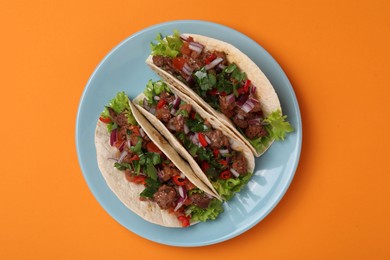 Delicious tacos with meat and vegetables on orange table, top view