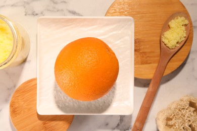 Photo of Orange, natural body scrub and luffa on white marble table, flat lay. Anti cellulite treatment