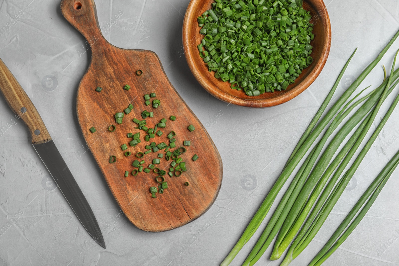 Photo of Flat lay composition with green onions, knife and bowl on grey stone table