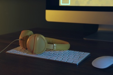 Photo of Modern headphones and computer with video game on table