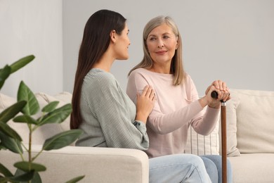 Mature lady with walking cane and young woman on sofa at home