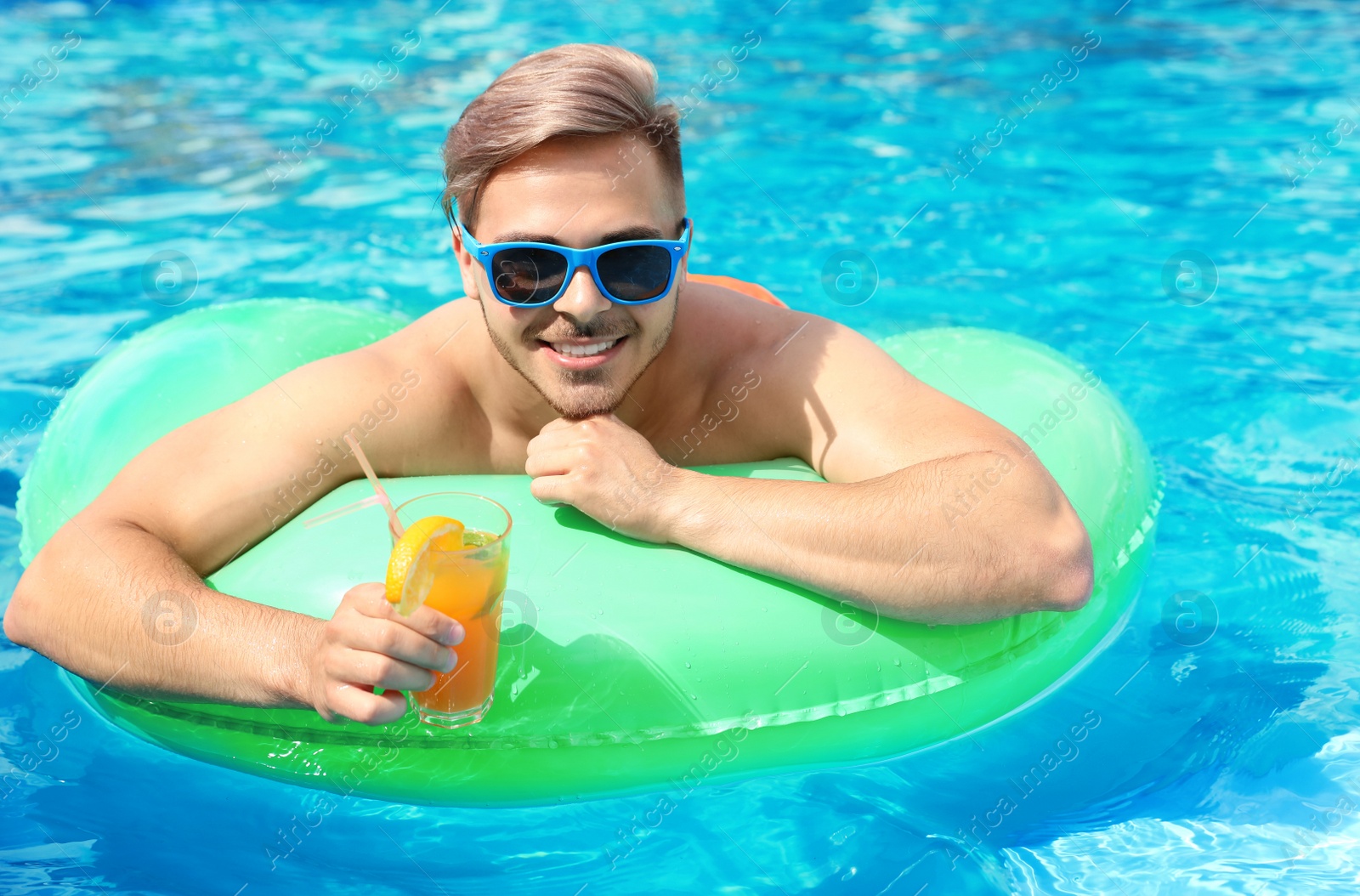 Photo of Young man with cocktail in pool on sunny day