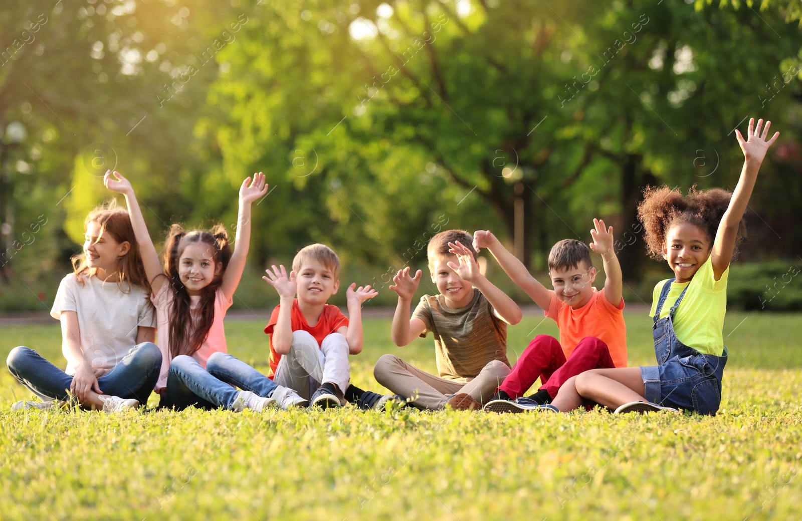 Photo of Cute little children sitting on grass outdoors on sunny day