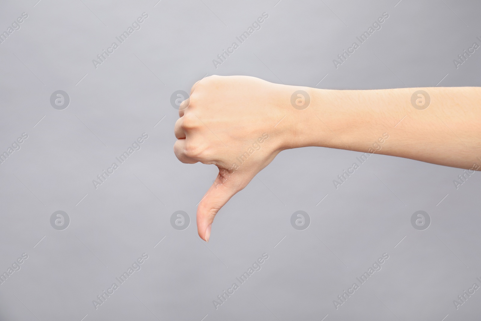 Photo of Woman showing thumb down sign on grey background, closeup. Body language