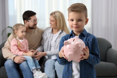 Photo of Family budget. Little boy with piggy bank, his parents and sister at home, selective focus