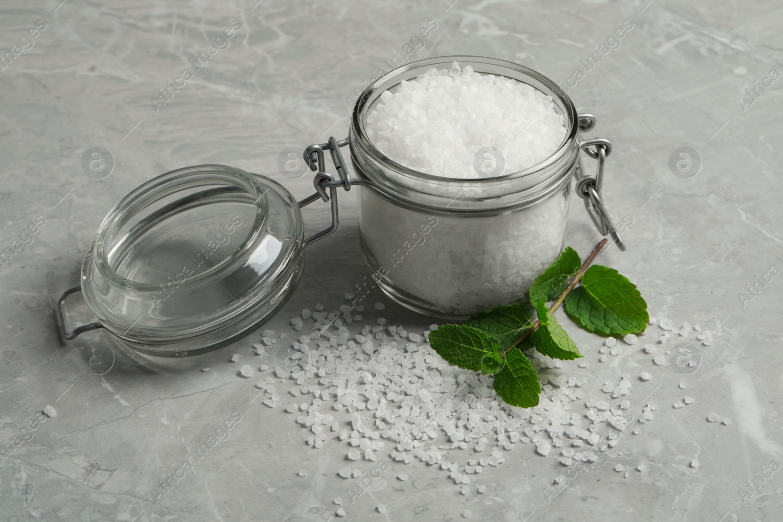 Photo of Natural sea salt in glass jar and mint on light grey marble table