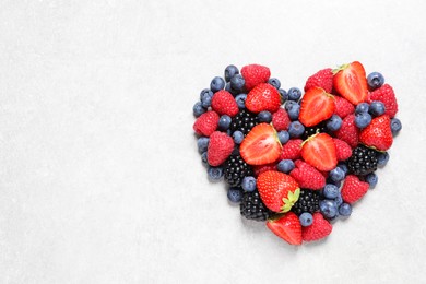 Photo of Heart made of different fresh ripe berries on white textured table, top view. Space for text