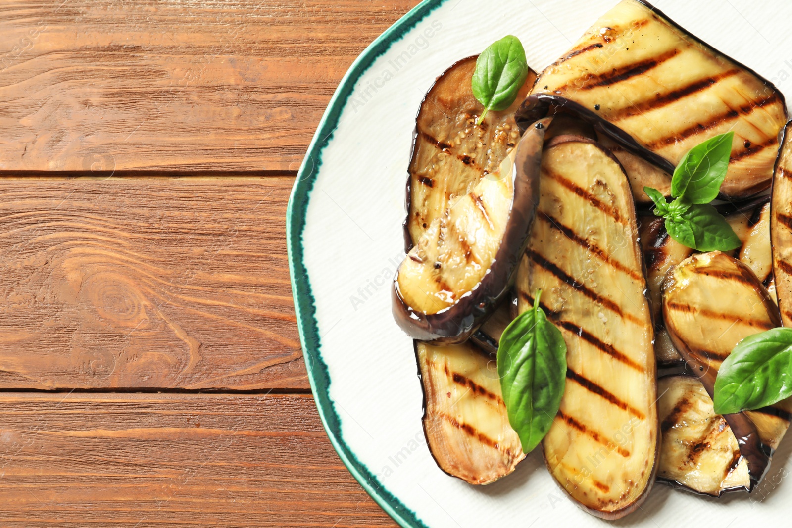 Photo of Plate with fried eggplant slices on wooden table, top view. Space for text