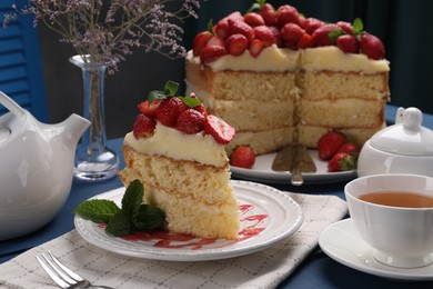 Photo of Piece of tasty cake with fresh strawberries, mint and cup of tea on blue wooden table