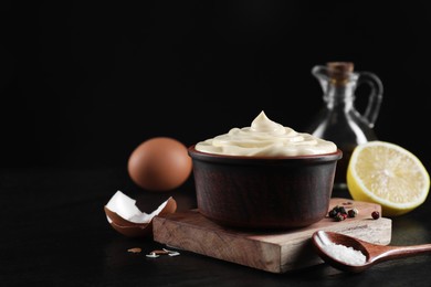 Photo of Fresh mayonnaise sauce in bowl and ingredients on black table, closeup. Space for text