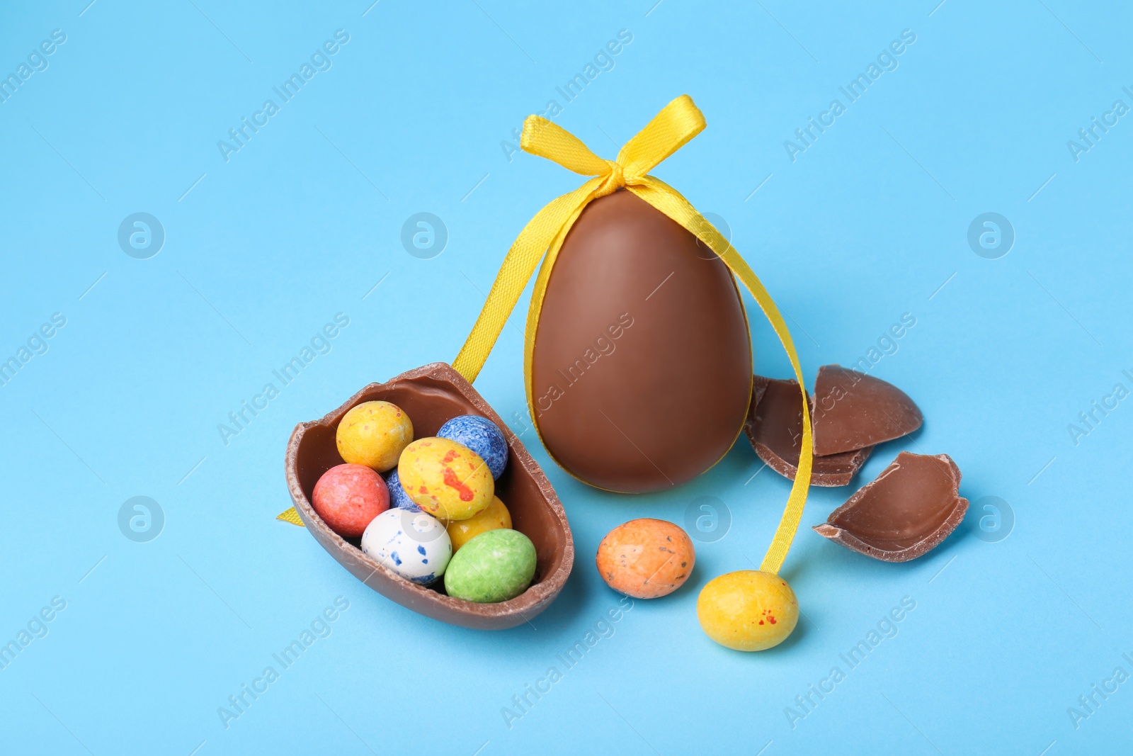 Photo of Tasty whole chocolate eggs with yellow bow and different candies on light blue background